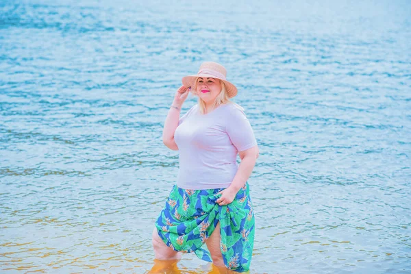 Artı plajda bir model. Şişman kadın hayattan zevk alıyor. Nehir kenarındaki doğada, kumların üzerinde dinlenen güzel bir kadın. Kadın hayatı kavramı.