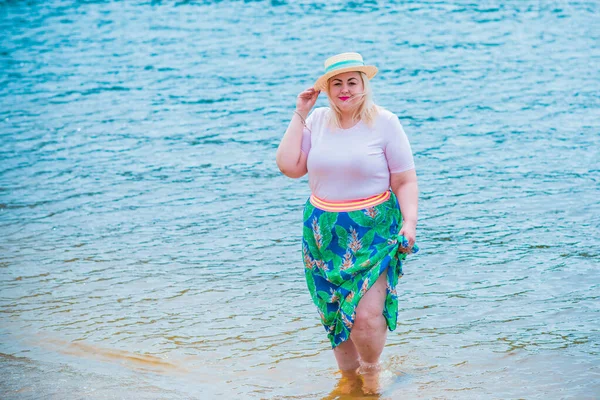 Artı plajda bir model. Şişman kadın hayattan zevk alıyor. Nehir kenarındaki doğada, kumların üzerinde dinlenen güzel bir kadın. Kadın hayatı kavramı.