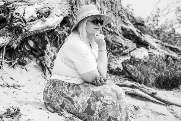 Artı plajda bir model. Şişman kadın hayattan zevk alıyor. Nehir kenarındaki doğada, kumların üzerinde dinlenen güzel bir kadın. Kadın hayatı kavramı.