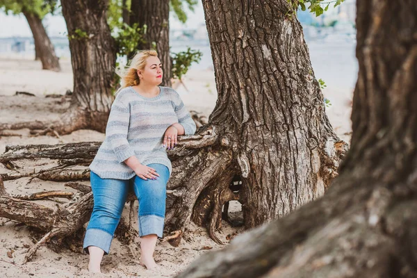 Artı plajda bir model. Şişman kadın hayattan zevk alıyor. Nehir kenarındaki doğada, kumların üzerinde dinlenen güzel bir kadın. Kadın hayatı kavramı.