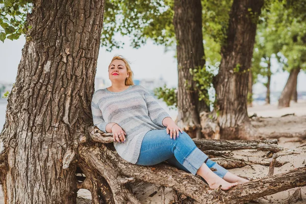 Artı plajda bir model. Şişman kadın hayattan zevk alıyor. Nehir kenarındaki doğada, kumların üzerinde dinlenen güzel bir kadın. Kadın hayatı kavramı.