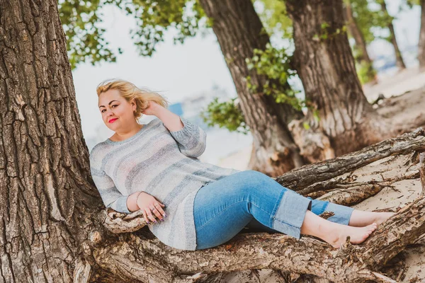 Artı plajda bir model. Şişman kadın hayattan zevk alıyor. Nehir kenarındaki doğada, kumların üzerinde dinlenen güzel bir kadın. Kadın hayatı kavramı.