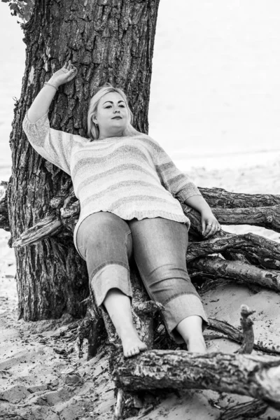 Artı plajda bir model. Şişman kadın hayattan zevk alıyor. Nehir kenarındaki doğada, kumların üzerinde dinlenen güzel bir kadın. Kadın hayatı kavramı.