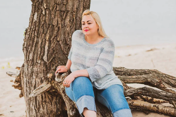 Artı plajda bir model. Şişman kadın hayattan zevk alıyor. Nehir kenarındaki doğada, kumların üzerinde dinlenen güzel bir kadın. Kadın hayatı kavramı.