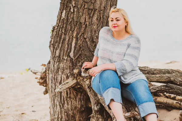 Artı plajda bir model. Şişman kadın hayattan zevk alıyor. Nehir kenarındaki doğada, kumların üzerinde dinlenen güzel bir kadın. Kadın hayatı kavramı.