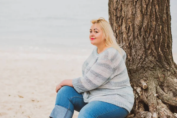 Artı plajda bir model. Şişman kadın hayattan zevk alıyor. Nehir kenarındaki doğada, kumların üzerinde dinlenen güzel bir kadın. Kadın hayatı kavramı.