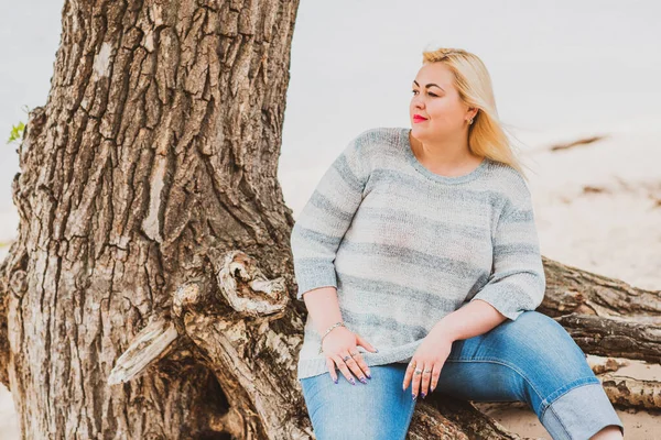 Artı plajda bir model. Şişman kadın hayattan zevk alıyor. Nehir kenarındaki doğada, kumların üzerinde dinlenen güzel bir kadın. Kadın hayatı kavramı.