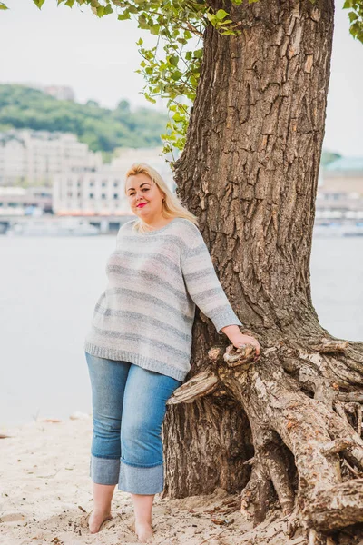 Artı plajda bir model. Şişman kadın hayattan zevk alıyor. Nehir kenarındaki doğada, kumların üzerinde dinlenen güzel bir kadın. Kadın hayatı kavramı.