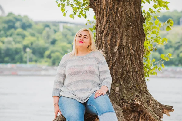 Artı plajda bir model. Şişman kadın hayattan zevk alıyor. Nehir kenarındaki doğada, kumların üzerinde dinlenen güzel bir kadın. Kadın hayatı kavramı.