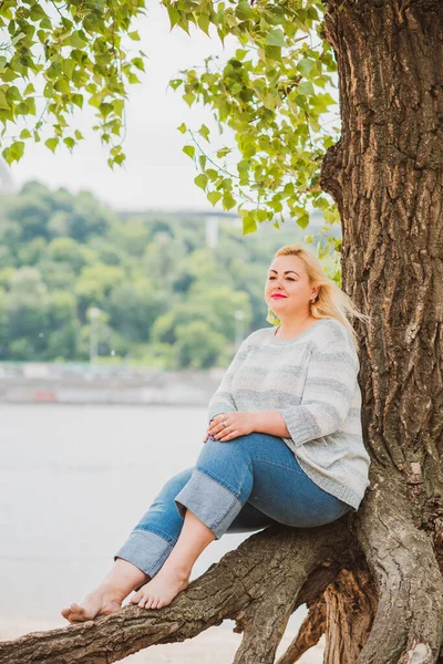 Artı plajda bir model. Şişman kadın hayattan zevk alıyor. Nehir kenarındaki doğada, kumların üzerinde dinlenen güzel bir kadın. Kadın hayatı kavramı.