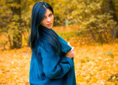 Sonbahar mavisi büyük montlu güzel bir kadının portresi. Esmer moda kadını, sonbahar manzarasına karşı yürüyordu. Zarif bir kadının moda fotoğrafıydı.  