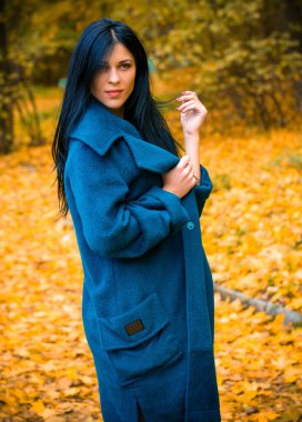 Sonbahar mavisi büyük montlu güzel bir kadının portresi. Esmer moda kadını, sonbahar manzarasına karşı yürüyordu. Zarif bir kadının moda fotoğrafıydı.  