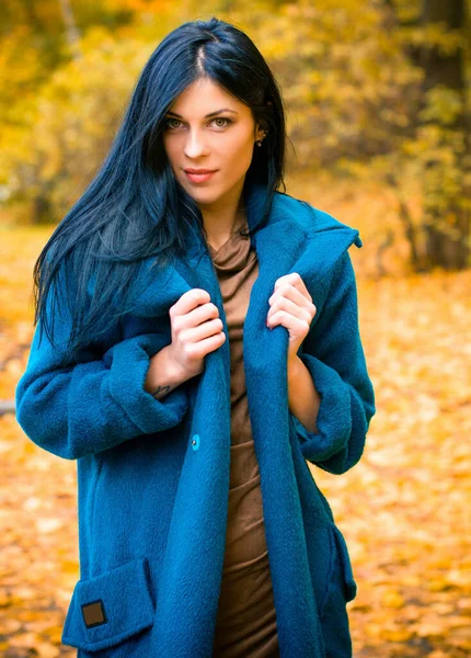 Portrait of young beautiful woman in autumn blue oversize coat. Brunette fashion woman walking outdoor against an autumn nature landscape High fashion photo of elegant woman stylish