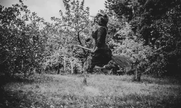 若い美しく神秘的な魔女の女性が森の中のブルームを飛んでいます 帽子の魔女は自由空間のほうきで飛ぶ ハロウィーンの休日魔法 — ストック写真