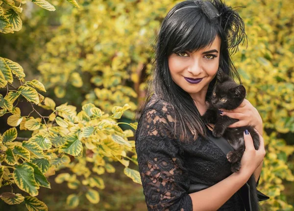 Cadılar Bayramı partisi konsepti, siyah kedili gizemli kız. Güzel, genç, karanlık cadı kadın. Cadılar Bayramı kutlamaları için ilham, fikirler ve basit detaylar.