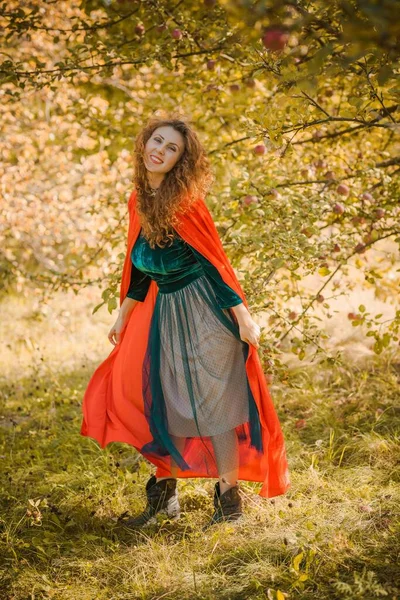 緑のベルベットのロマンチックなドレスと赤のフード 女の子のためのハロウィンスタイル 背景で秋の自然 — ストック写真