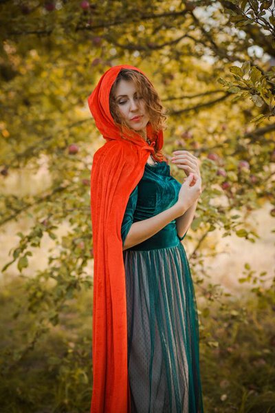 Woman in green velvet romantic dress and red hood, Halloween style for girls, autumn nature at background