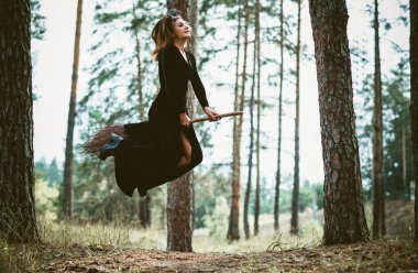 Genç, güzel ve gizemli cadı kadın ormanda Broom 'da uçuyor. Havalanma, süpürgede bir cadı, boş yer. Cadılar Bayramı tatili, sihir