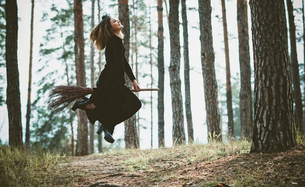 若い美しく神秘的な魔女の女性が森の中のブルームを飛んでいます 帽子の魔女は自由空間のほうきで飛ぶ ハロウィーンの休日魔法 — ストック写真