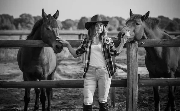 American woman on a horse farm. Portrait of girl in cowboy hat with a  horses. Hippotherapy at nature