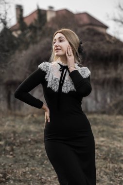 Klasik siyah uzun elbiseli, boynunda beyaz dantelli orta yaşlı bir bayan. Şık kıyafet.