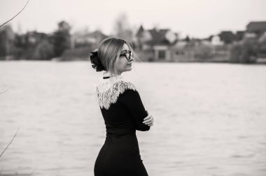 Klasik siyah uzun elbiseli, boynunda beyaz dantelli orta yaşlı bir bayan. Şık kıyafet.