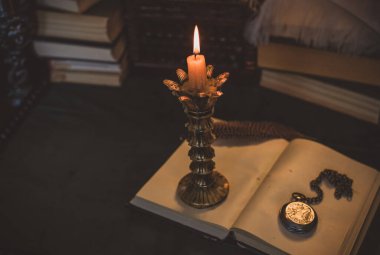 Eskimiş bir masada kitap ve mum, karanlık akademi estetiği. Akşam vakti.