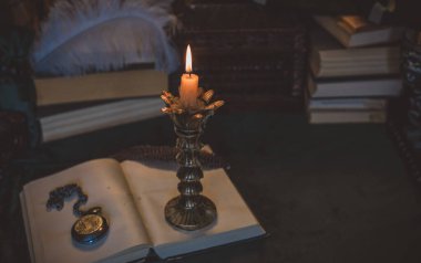Eskimiş bir masada kitap ve mum, karanlık akademi estetiği. Akşam vakti.