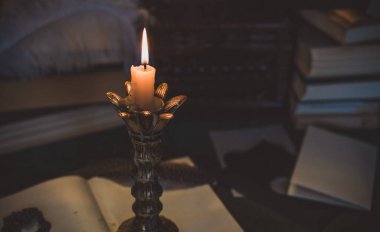 Eskimiş bir masada kitap ve mum, karanlık akademi estetiği. Akşam vakti.
