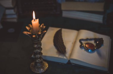 Eskimiş bir masada kitap ve mum, karanlık akademi estetiği. Akşam vakti.