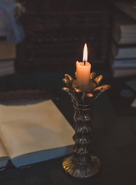 Eskimiş bir masada kitap ve mum, karanlık akademi estetiği. Akşam vakti.