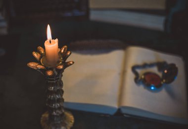 Eskimiş bir masada kitap ve mum, karanlık akademi estetiği. Akşam vakti.