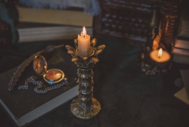 Eskimiş bir masada kitap ve mum, karanlık akademi estetiği. Akşam vakti.