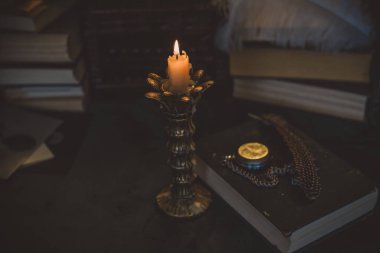 Eskimiş bir masada kitap ve mum, karanlık akademi estetiği. Akşam vakti.