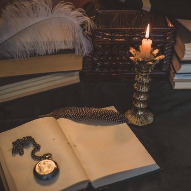 Eskimiş bir masada kitap ve mum, karanlık akademi estetiği. Akşam vakti.