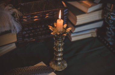 Eskimiş bir masada kitap ve mum, karanlık akademi estetiği. Akşam vakti.