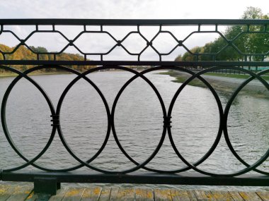 Köprünün dökme demir kafes deseninin bir parçası. Su ve sonbahar ağaçlarının yapraklarına yakın plan..