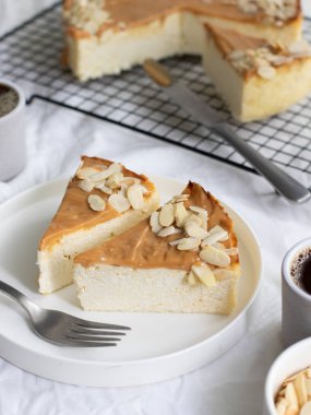 İki dilim ev yapımı peynirli kek, konsantre süt ve kahveyle servis edilen badem gevreği. Arkasında fırında bir cheesecake var.