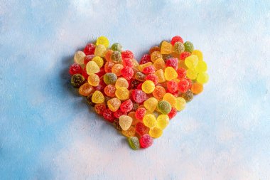 Açık mavi arka planda renkli ekşi şekerler. Kalp şekli renkli ve lezzetli şekerlemelerle yaratıldı