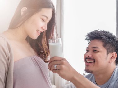 Asyalı adam Asyalı hamile karısıyla ilgileniyor. Genç hamile kadın süt içiyor..