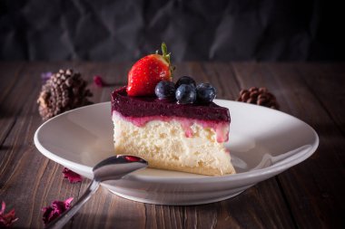 Yaban mersinli cheesecake ahşap tahtada kozalaklı ve kuru çiçekle süslenir.
