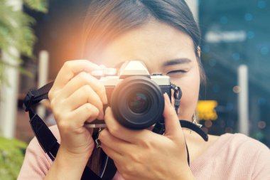 Retro film kamerası olan oldukça havalı bir Asyalı kadın ya da modern bahçe açık alışveriş merkezinde aynasız kamera. Genç kadın aynasız kamerayı klasik tonda tutuyor.;