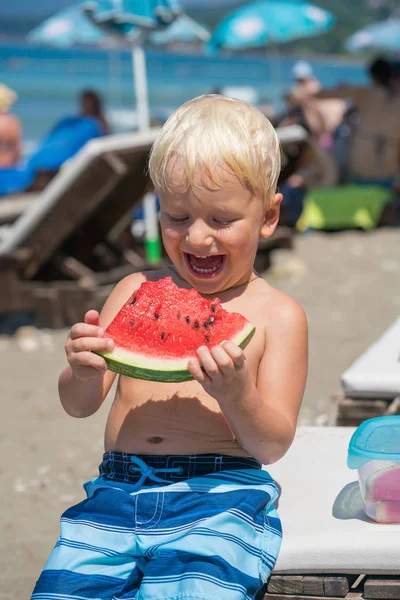Мальчик ест кусок арбуза на пляже — стоковое фото