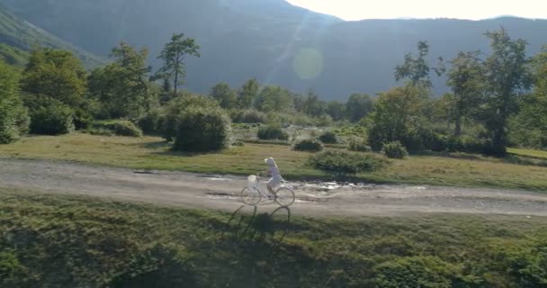 Foto van een jonge vrouw in een lichte jurk en hoed paardrijden fiets op het platteland weg — Stockvideo