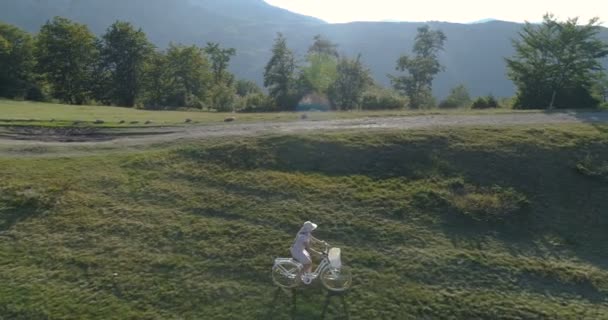 Foto van een jonge vrouw in een lichte jurk en hoed paardrijden fiets op het platteland weg — Stockvideo