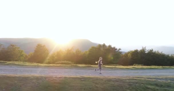 Frau läuft bei Sonnenuntergang auf Landstraße. — Stockvideo