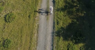 Kırsal yolda bisiklet süren, açık renk elbiseli ve şapkalı genç bir kadının fotoğrafı.