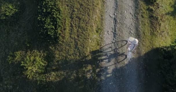 Tiro de uma jovem mulherem um vestido leve e chapéu andar de bicicleta na estrada rural — Vídeo de Stock