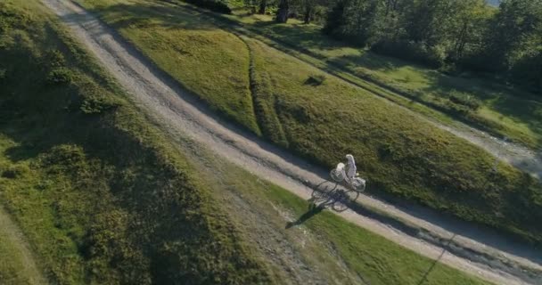 Tiro de uma jovem mulherem um vestido leve e chapéu andar de bicicleta na estrada rural — Vídeo de Stock