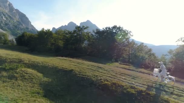 Foto van een jonge vrouw in een lichte jurk en hoed paardrijden fiets op het platteland weg — Stockvideo